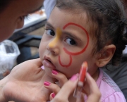 Profissional segurando rosto de criança por volta de três anos tendo o rosto pintado